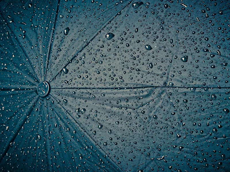 Foto eines geöffneten Regenschirms mit abperlenden Regentropfen als Zeichen des Schutzes