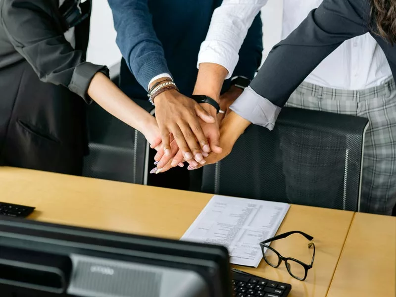 Vier Personen legen die Hände in der Mitte übereinander zur Symbolisierung der Teamarbeit.